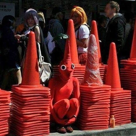 A guy dressed up as a cone sitting next to a bunch of real cones