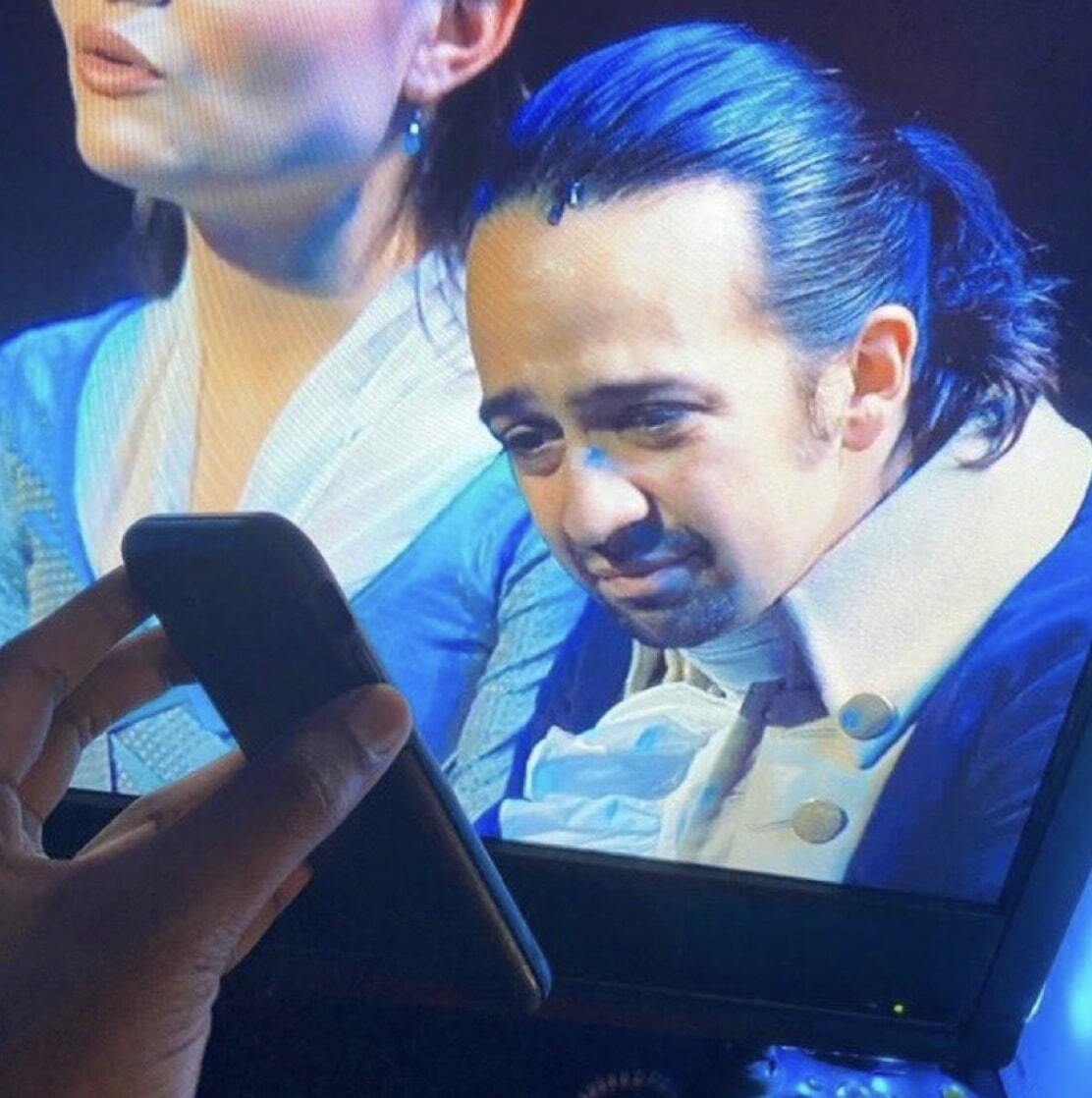 A hand holding up a phone to Hamilton's on a TV screen