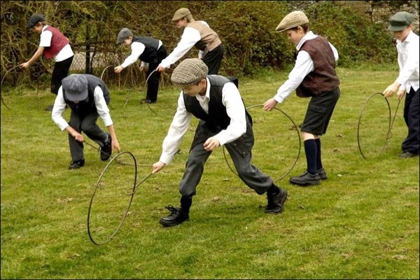 Boys rolling a hoop with a stick dressed in 19th Century clothes