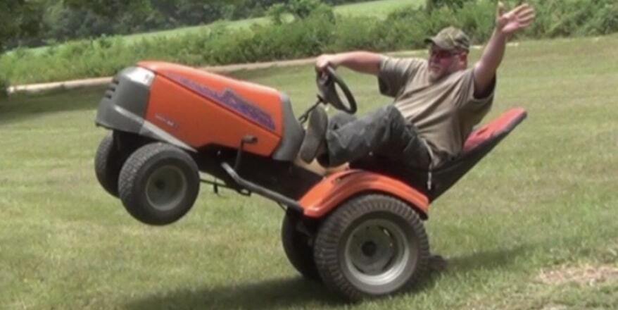 A guy popping a wheelie on his seated lawnmower