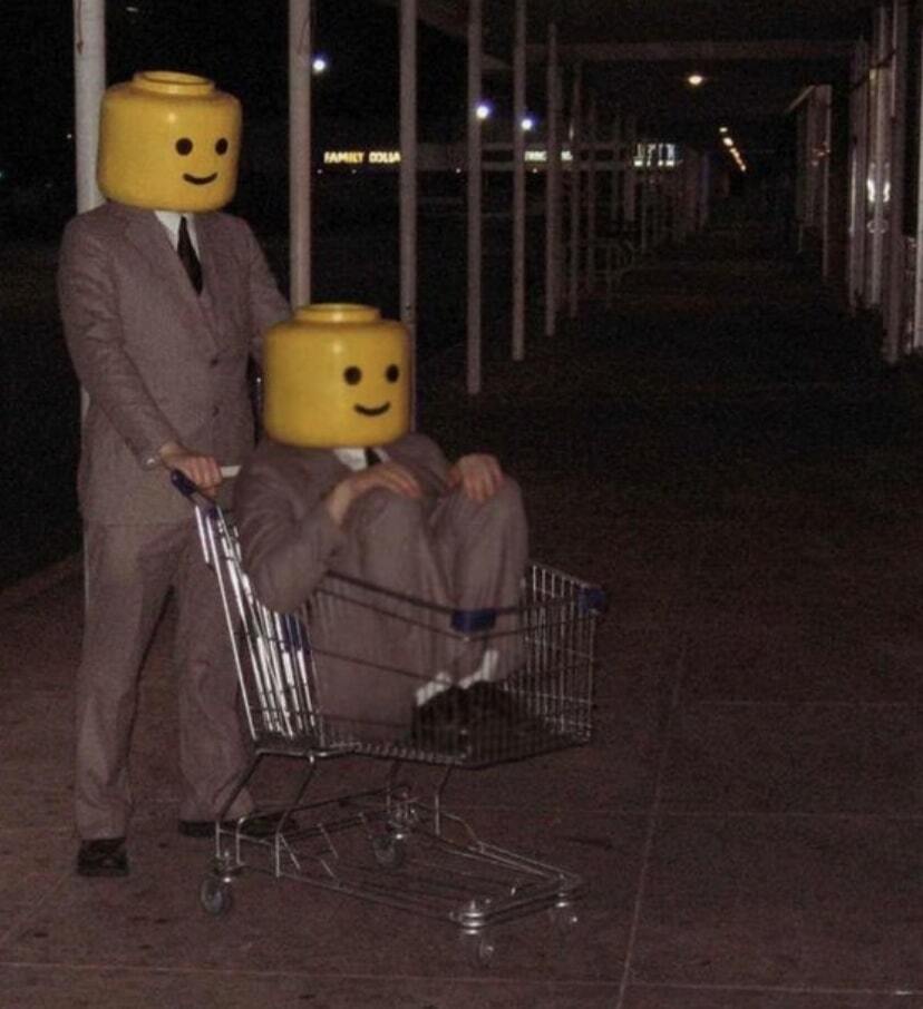 A guy with a lego head pushing another guy with a lego head in a shopping cart