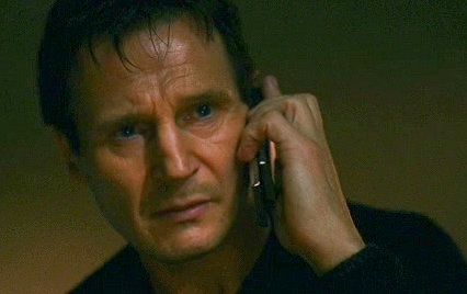 Liam Neeson holds a phone to his ear with a stern expression
