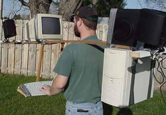 A guy walking in a yard with a desktop computer strapped to him