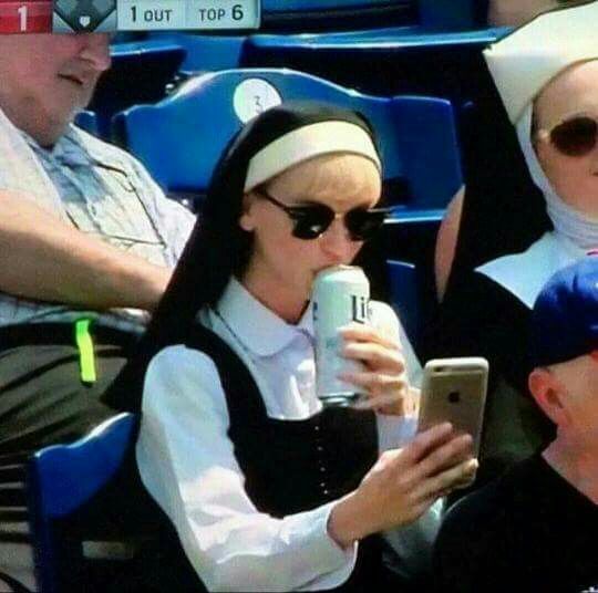 A nun taking a selfie holding a beer can at a baseball game