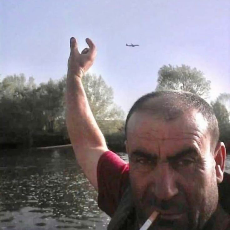 A man using forced perspective to hold his fingers an inch apart around a distant airplane