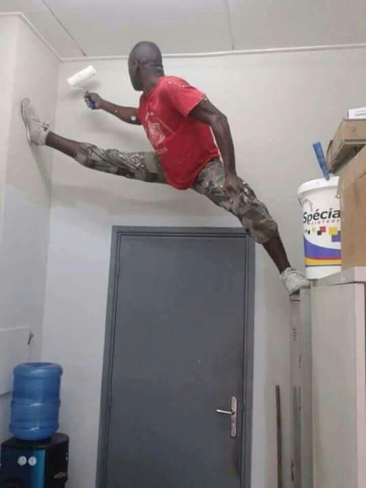 A painter doing the splits between two walls while painting a ceiling