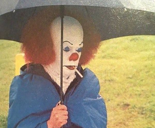 Pennywise the clown smoking under an umbrella