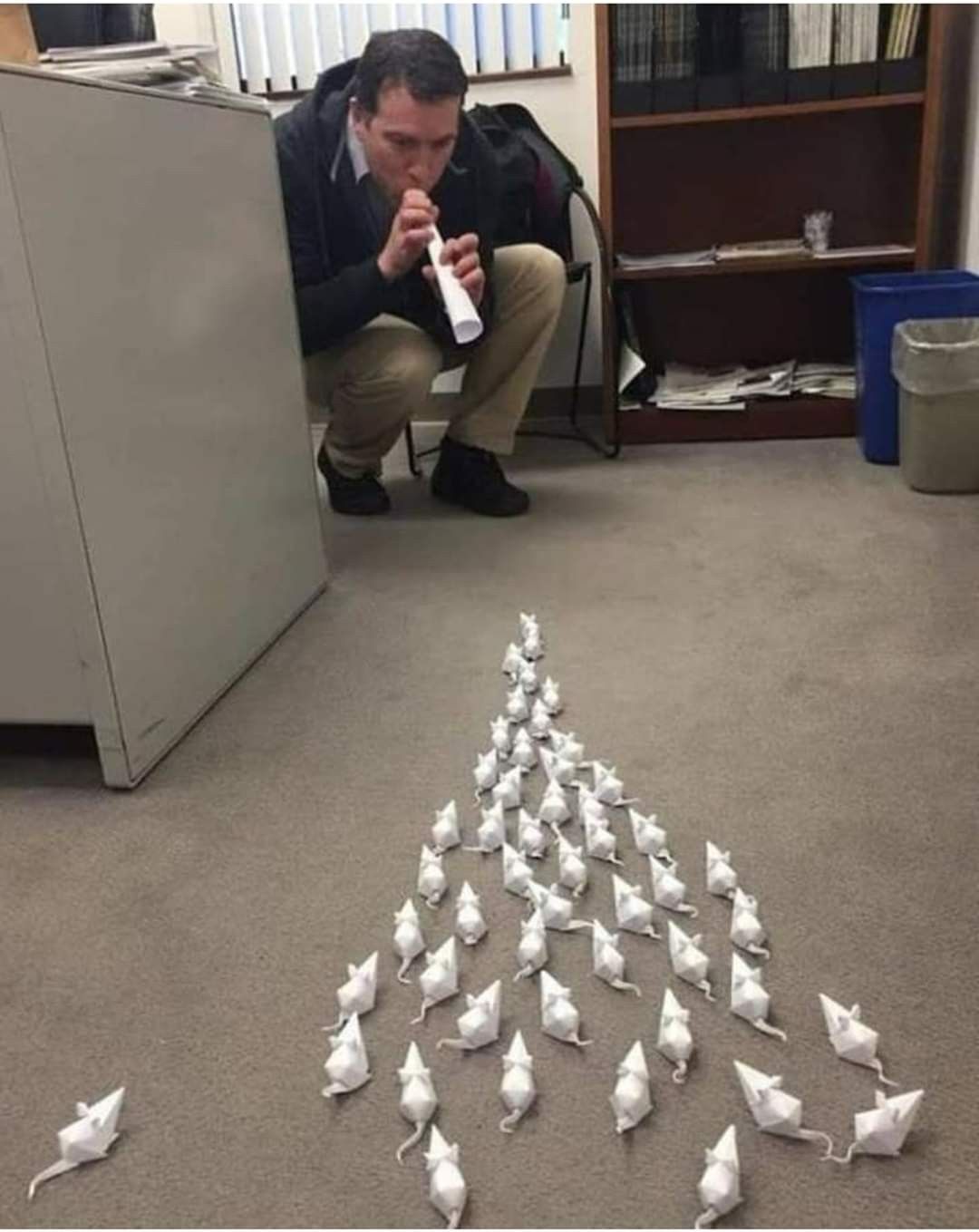 A guy playing a fake flute to a bunch of paper mice