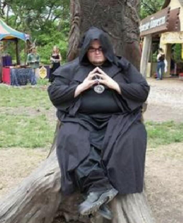 A guy dressed in a black robe at a renaissance fair looking very pleased