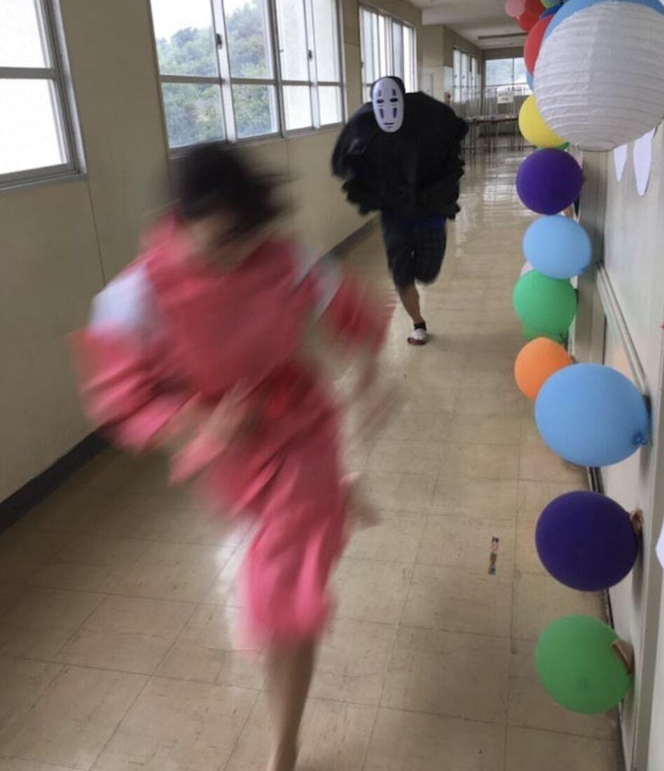 Girl running away from person dressed up as demon from Spirited Away