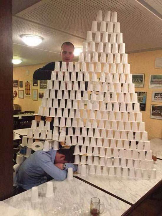 A guy stacking a bunch of plastic cups on top of a guy who's sleeping