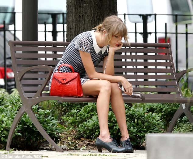 Taylor Swift looking sad sitting on a bench.