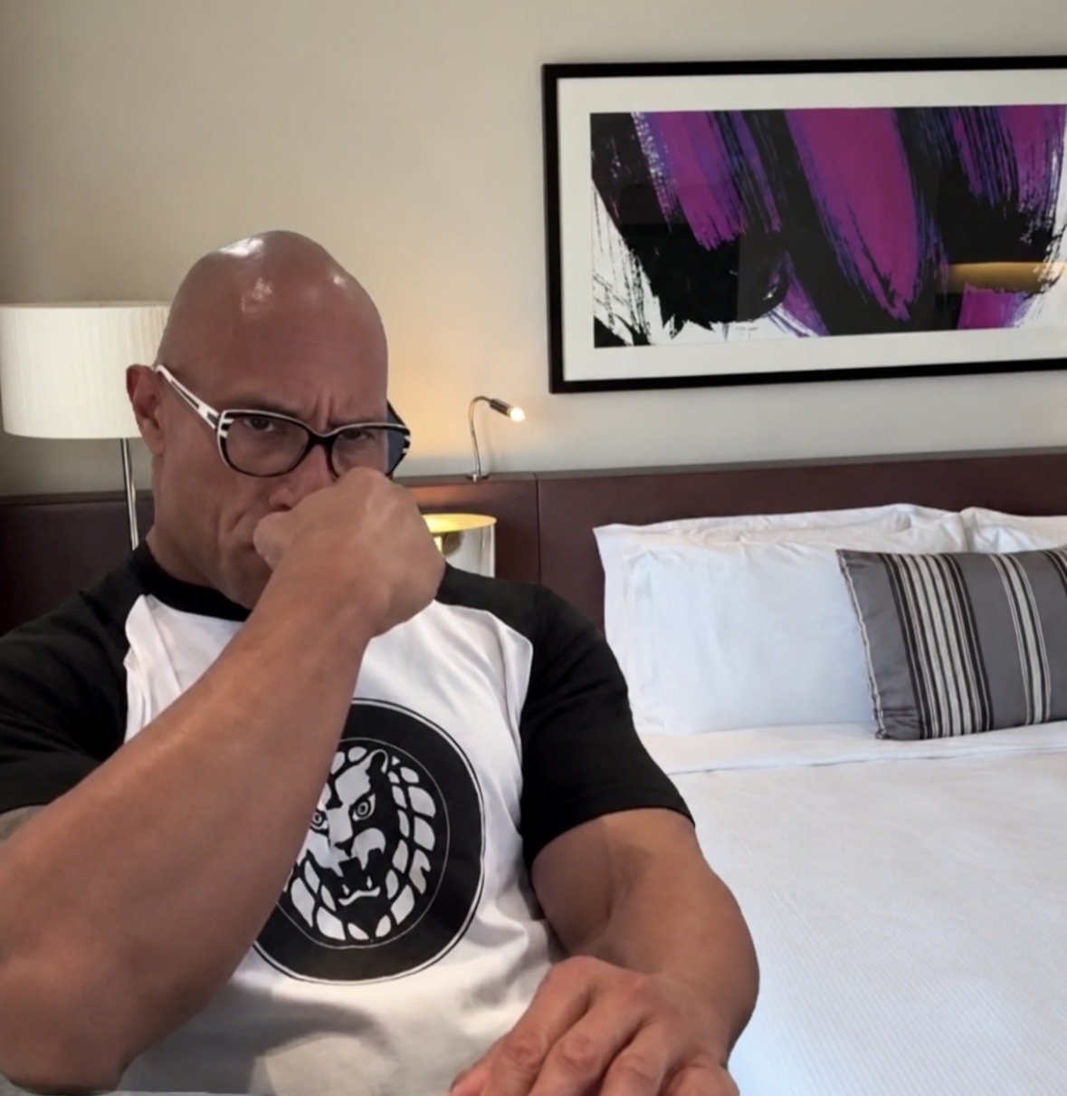The Rock wearing glasses and resting his fist against his mouth with a concerned expression