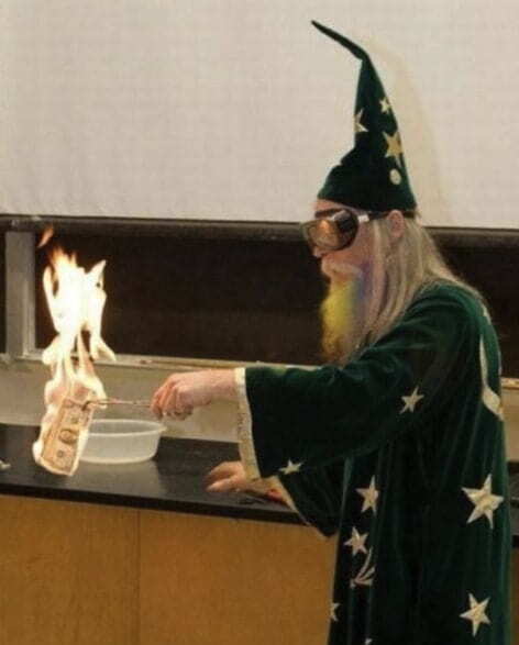 Old professor wearing a wizard costume and burning a dollar bill
